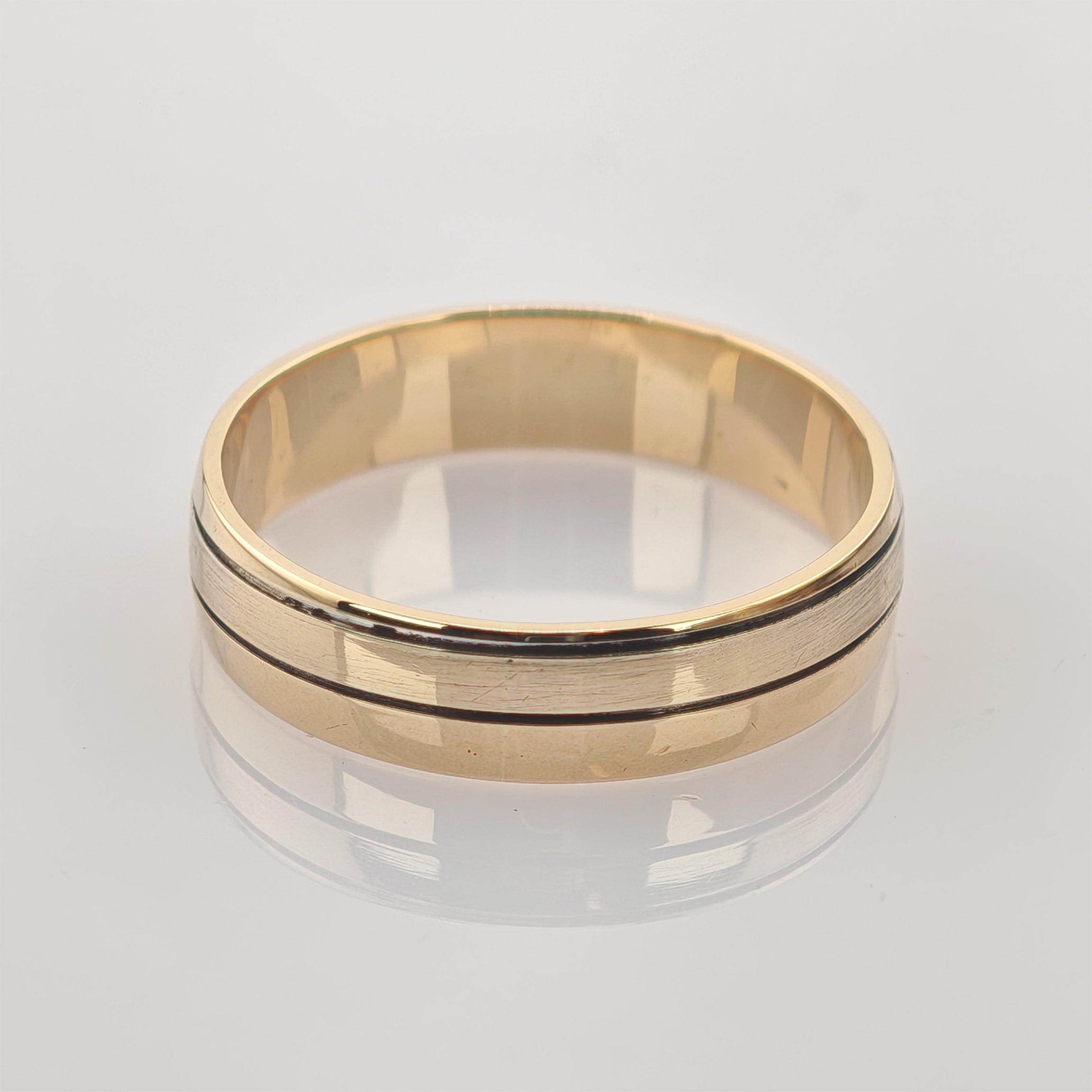 Goldfarbener Ring mit polierter Oberfläche und zwei dünnen parallelen Rillen auf spiegelnder weißer Fläche