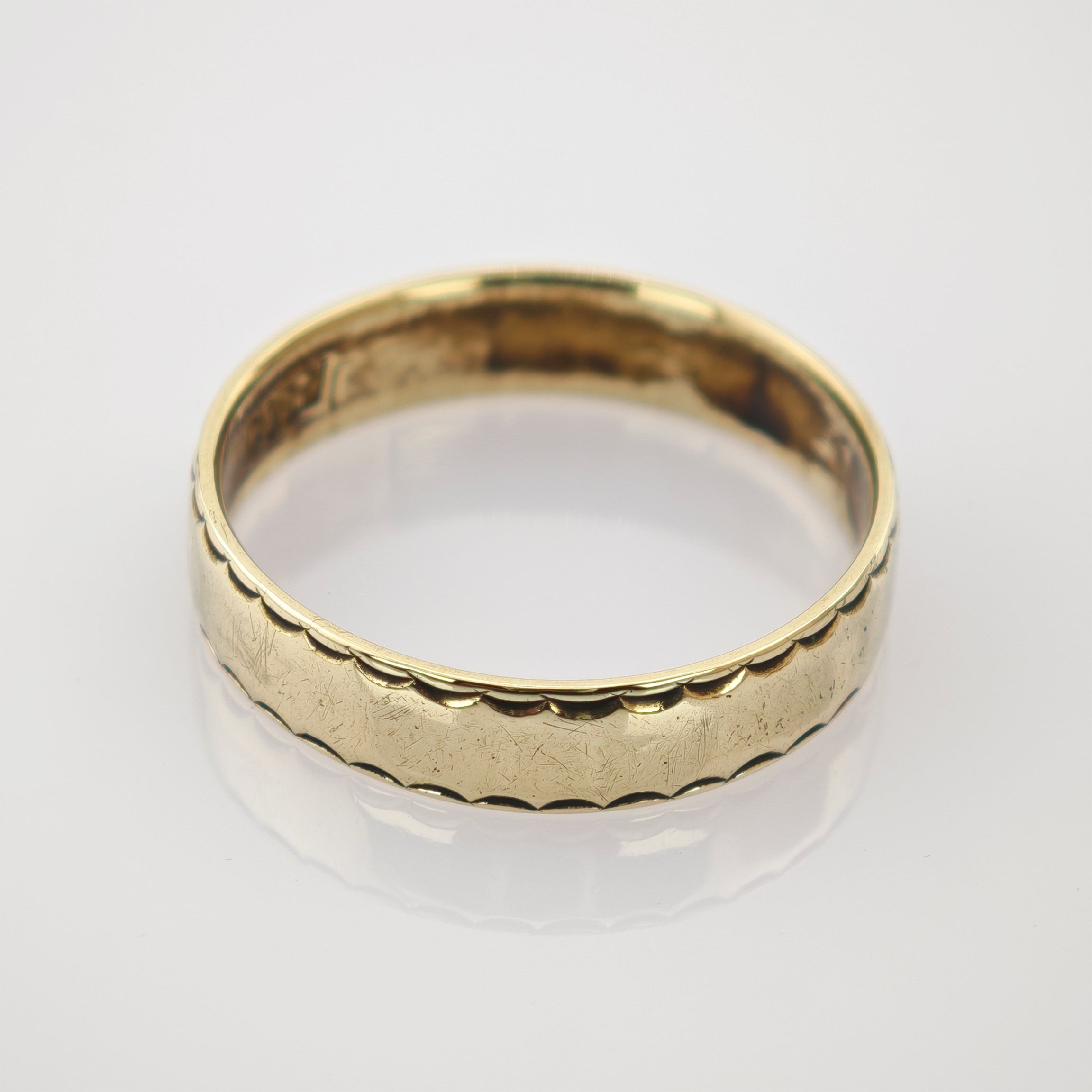 Goldring mit 18k Punze und welligem Rand auf reflektierendem Untergrund.