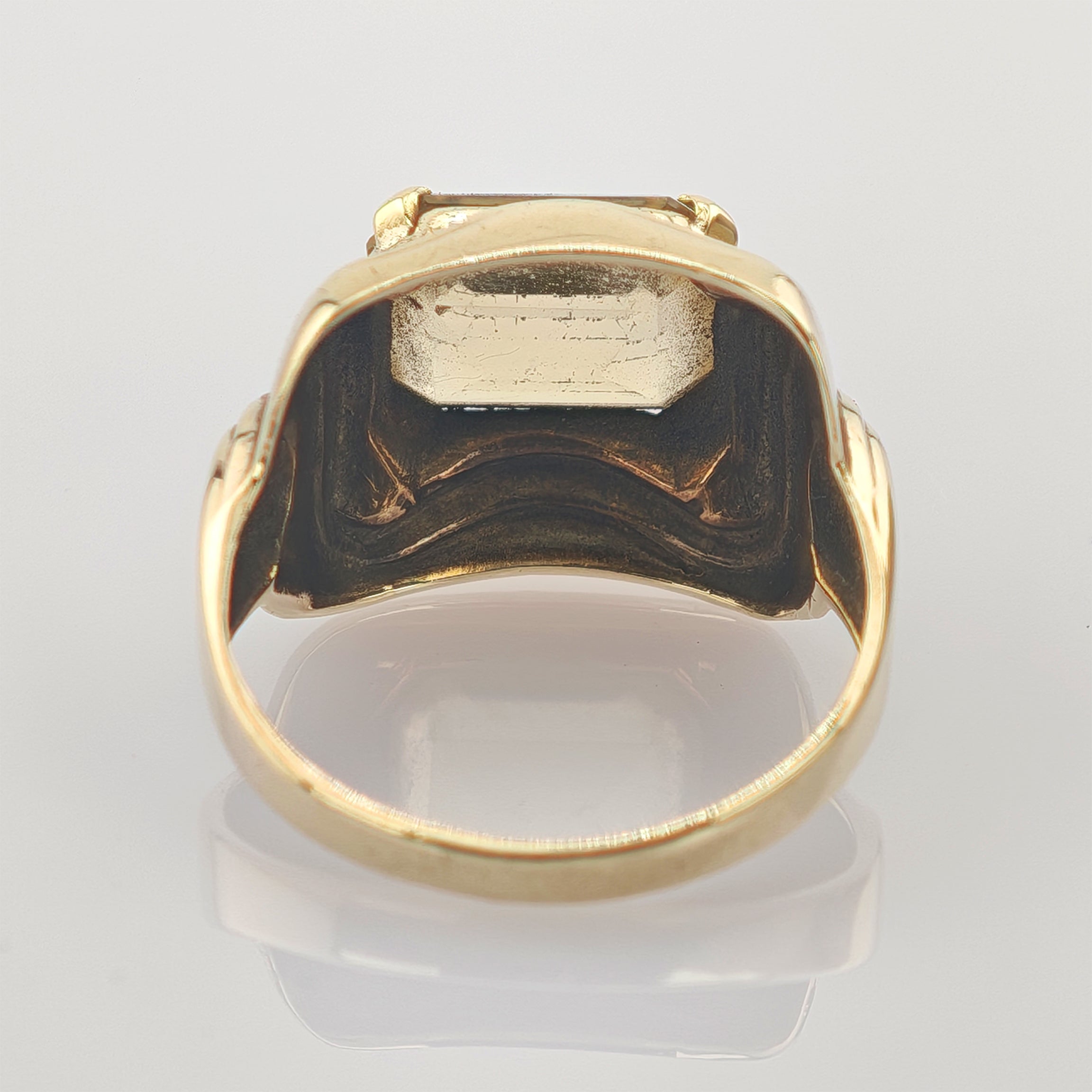 Nahaufnahme des inneren Rings eines 10-Karat-Gelbgoldrings mit eingravierten Stempeln auf neutralem Goldring mit detaillierter Gravur und Textur auf weißem, reflektierendem Untergrund