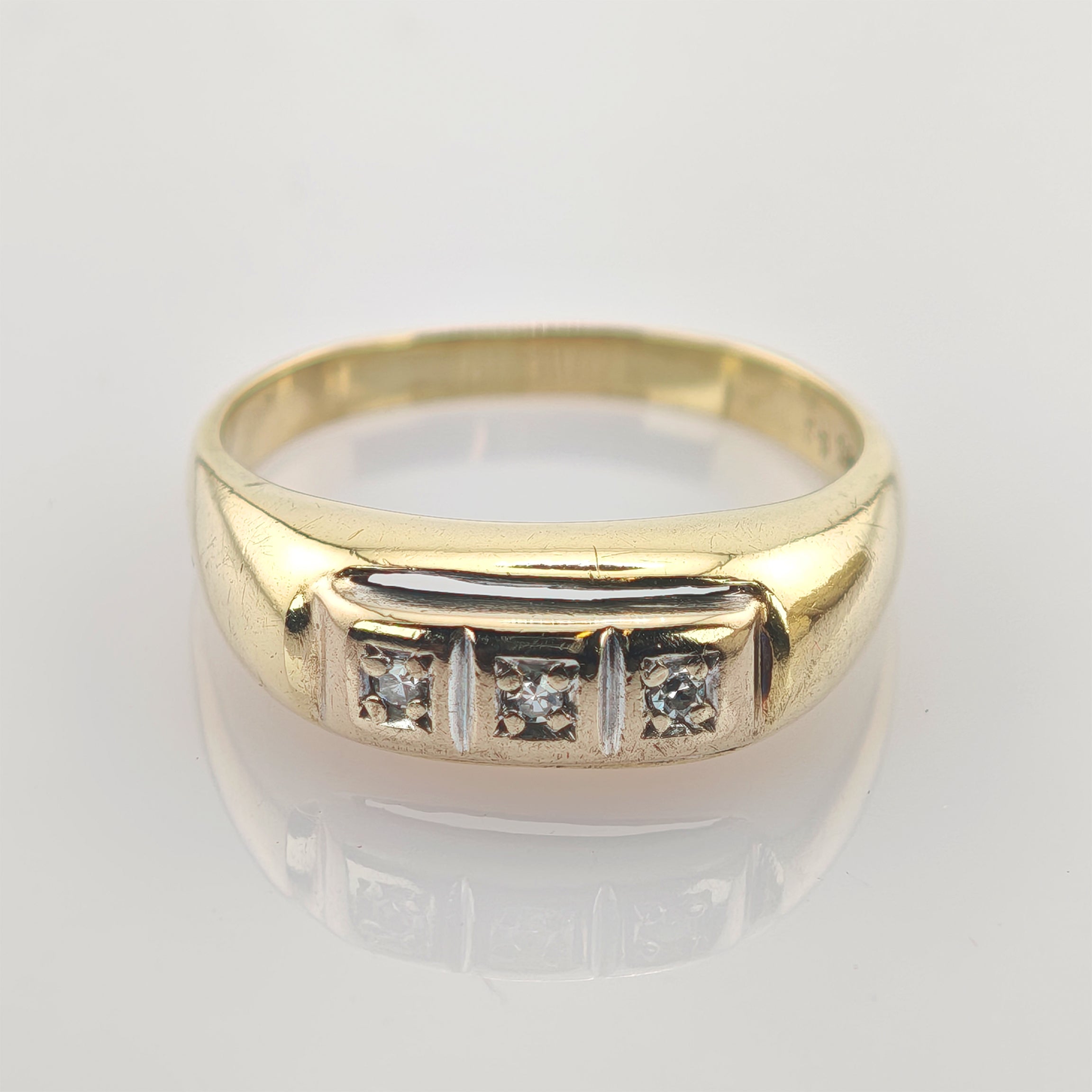 Goldring mit drei kleinen Diamanten in rechteckigen Fassungen auf polierter Oberfläche.