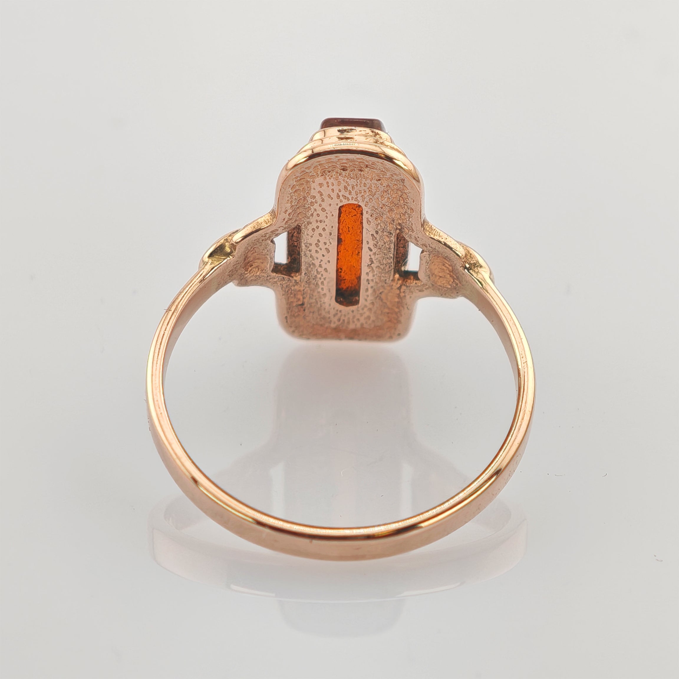 Goldring mit rechteckigem offenem Schlitz und rotem Edelstein auf hellgrauem Hintergrund.