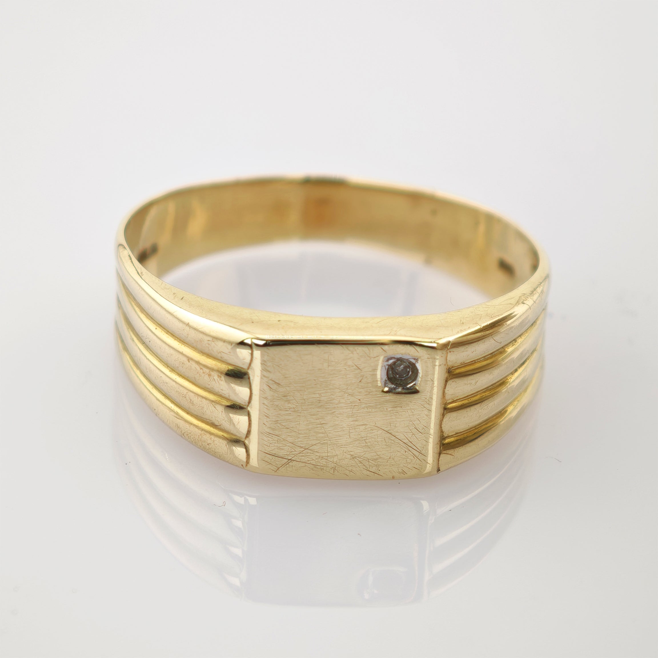 Goldener Ring mit rechteckigem Kopf und dunklem Stein, feine Gebrauchsspuren, drei Rillen am Band