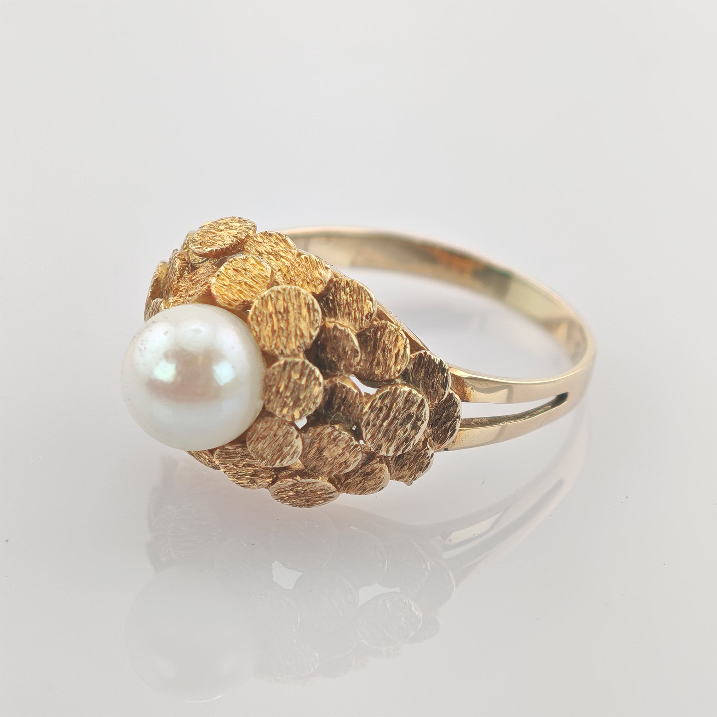 Goldring mit zentraler weißer Perle und strukturierten goldenen Scheiben in elegantem Design