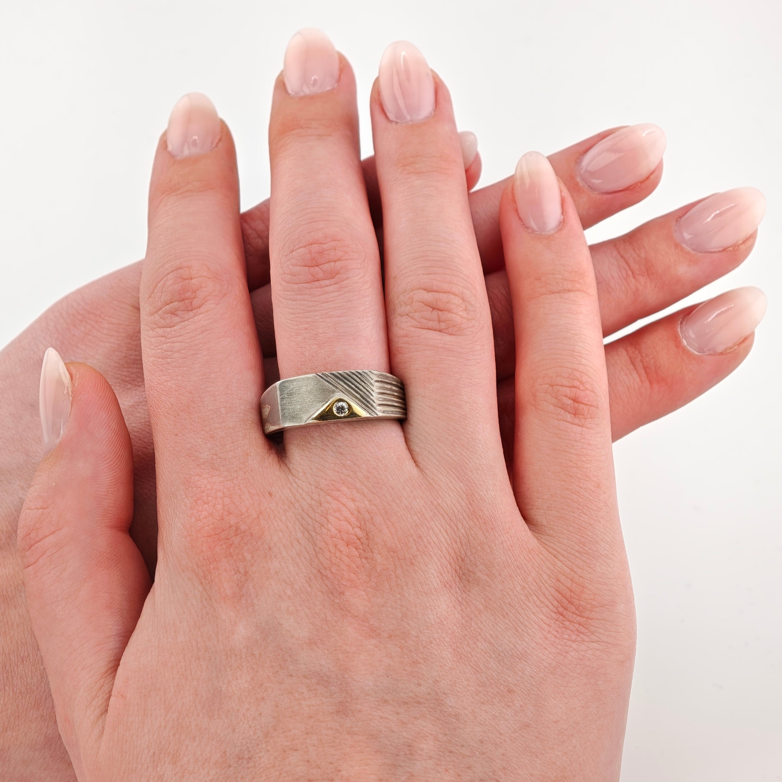 Zwei überlappende Hände mit silbernem Ring und kleinem Diamanten auf weißem Hintergrund.