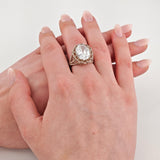 Zwei helle Hände, obere Hand trägt einen silbernen Ring mit gedrehtem Band und großem ovalem klarem Edelstein, gepflegte Nägel mit hellem rosa Nagellack.