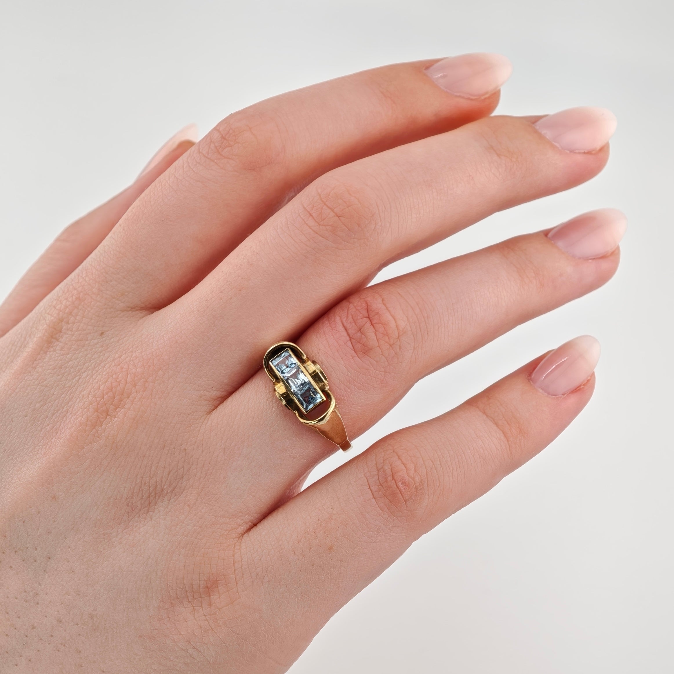 Hand mit gepflegten hellrosanen Nägeln und goldenem Ring mit drei blauen Edelsteinen