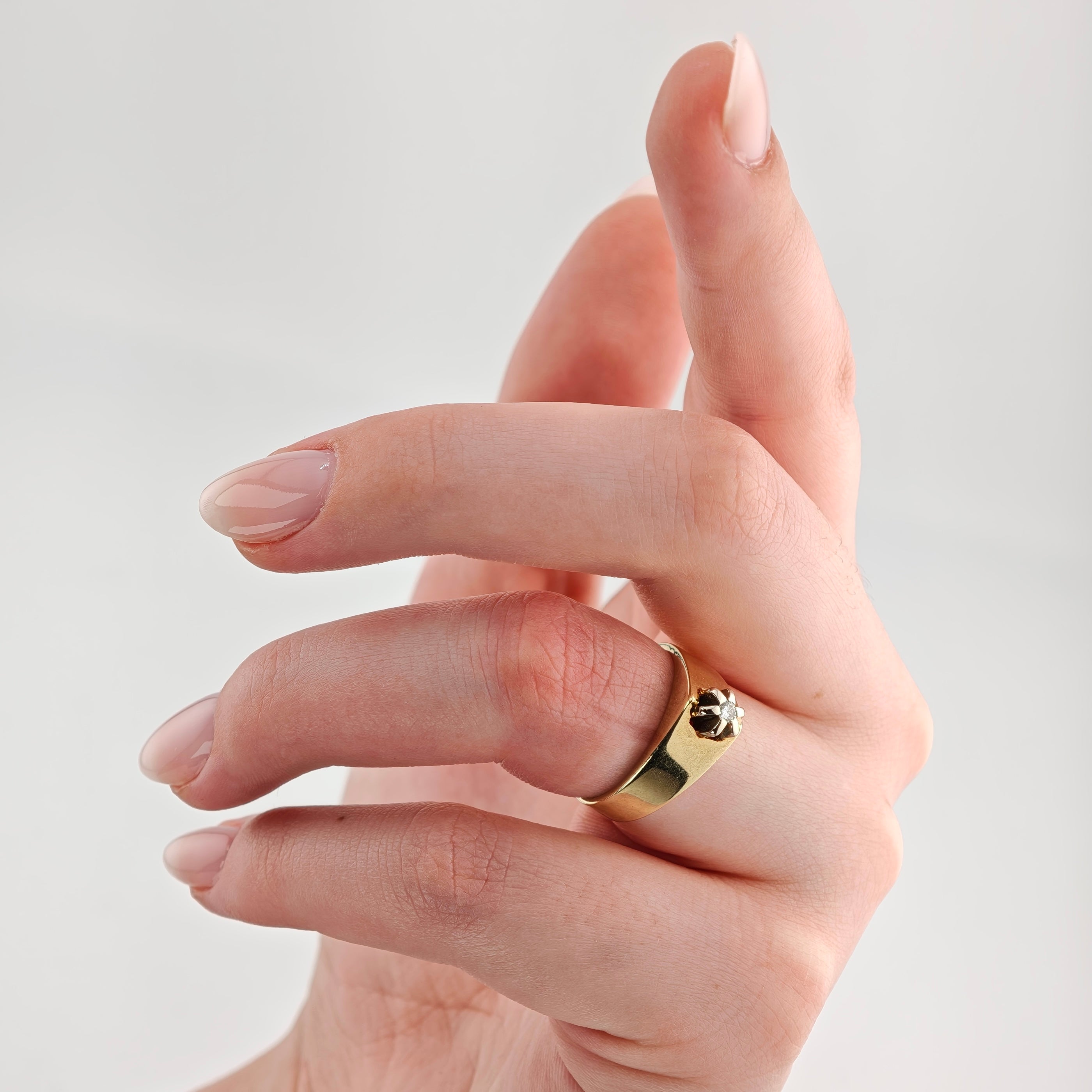 Hand mit gepflegten, hellrosa Nägeln trägt einen goldenen Ring mit kleinem Diamanten am Ringfinger