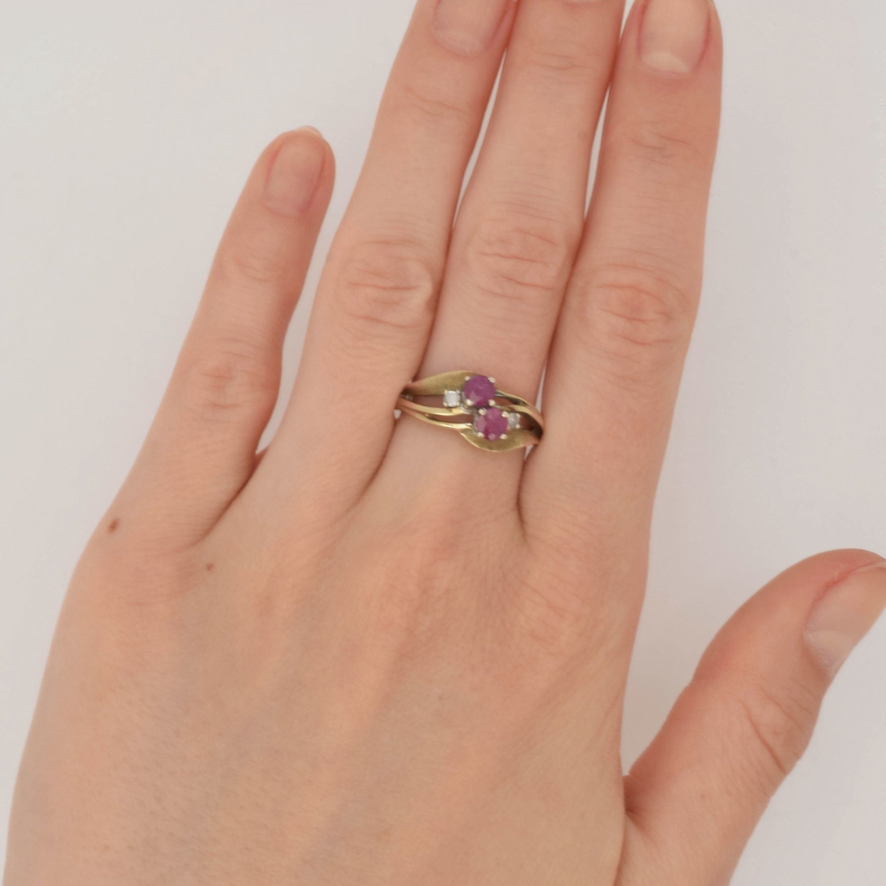 Hand mit goldfarbenem Ring und violetten Edelsteinen vor weißem Hintergrund