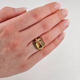 Hand mit gepflegten Nägeln, goldener Ring mit gelbem Edelstein auf neutralem Hintergrund