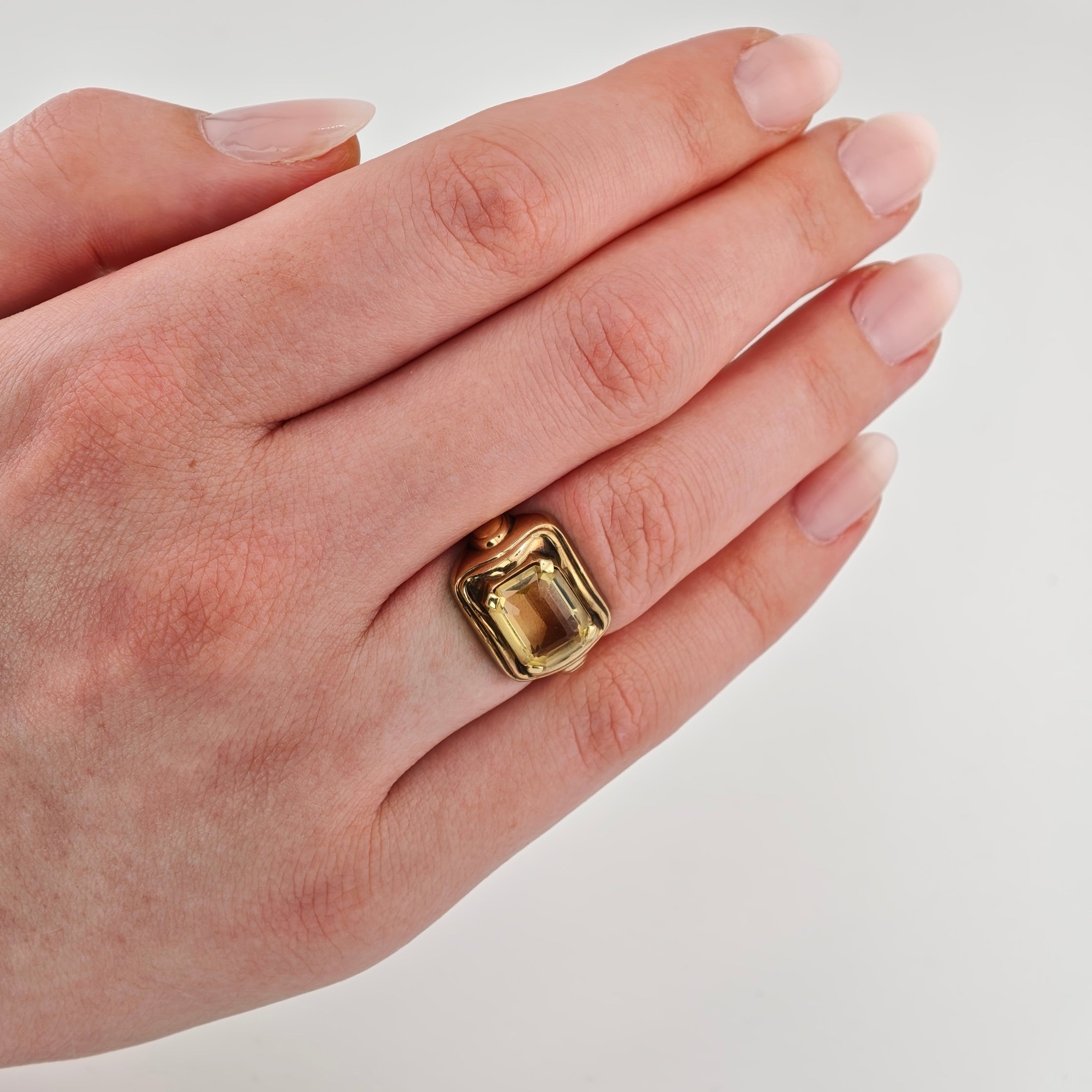 Hand mit gepflegten Nägeln, goldener Ring mit gelbem Edelstein auf neutralem Hintergrund