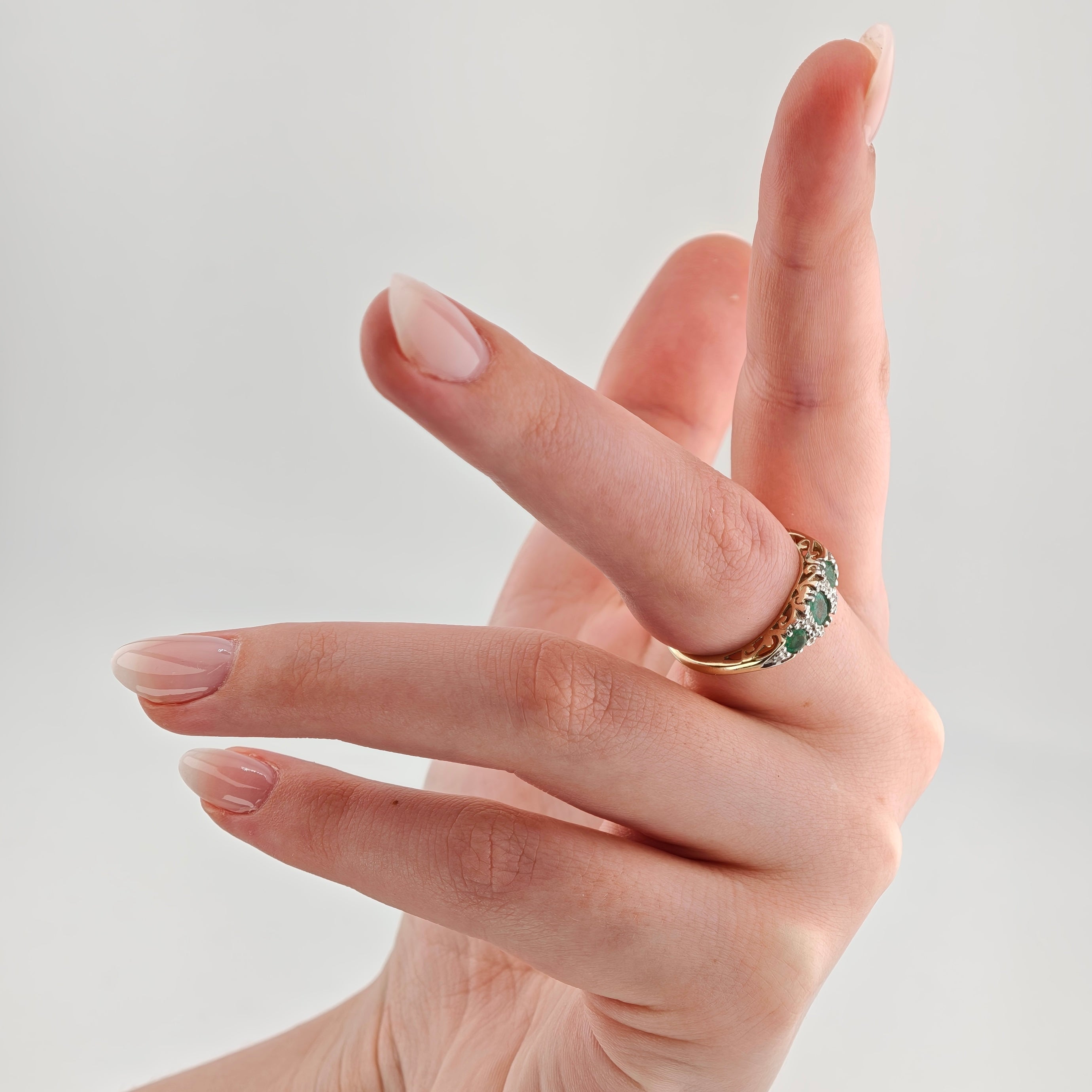 Hand mit Goldring und grünem Edelstein am Mittelfinger vor weißem Hintergrund