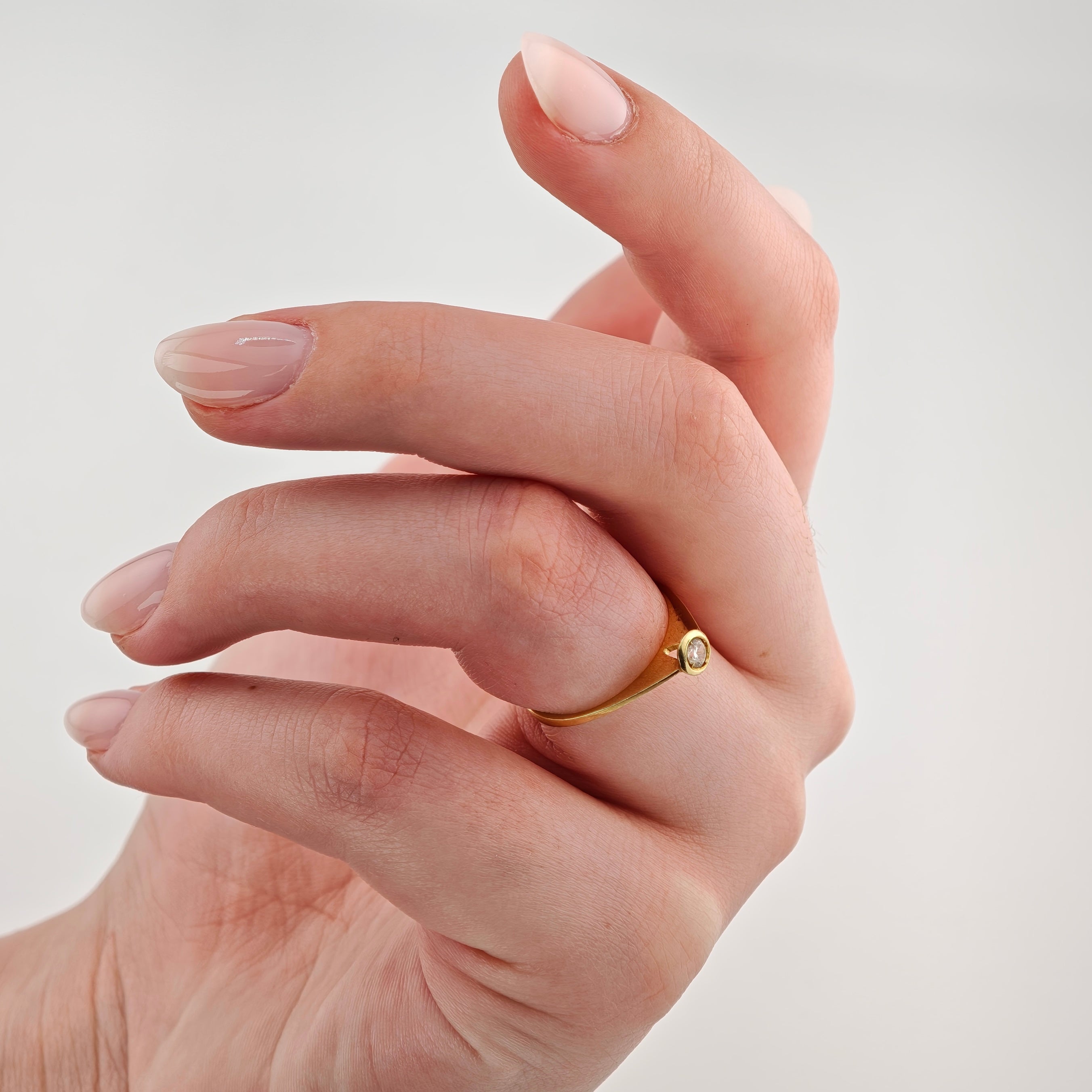 Hand mit hellem Hautton, zartrosa lackierten Nägeln und goldenem Ring mit Edelstein