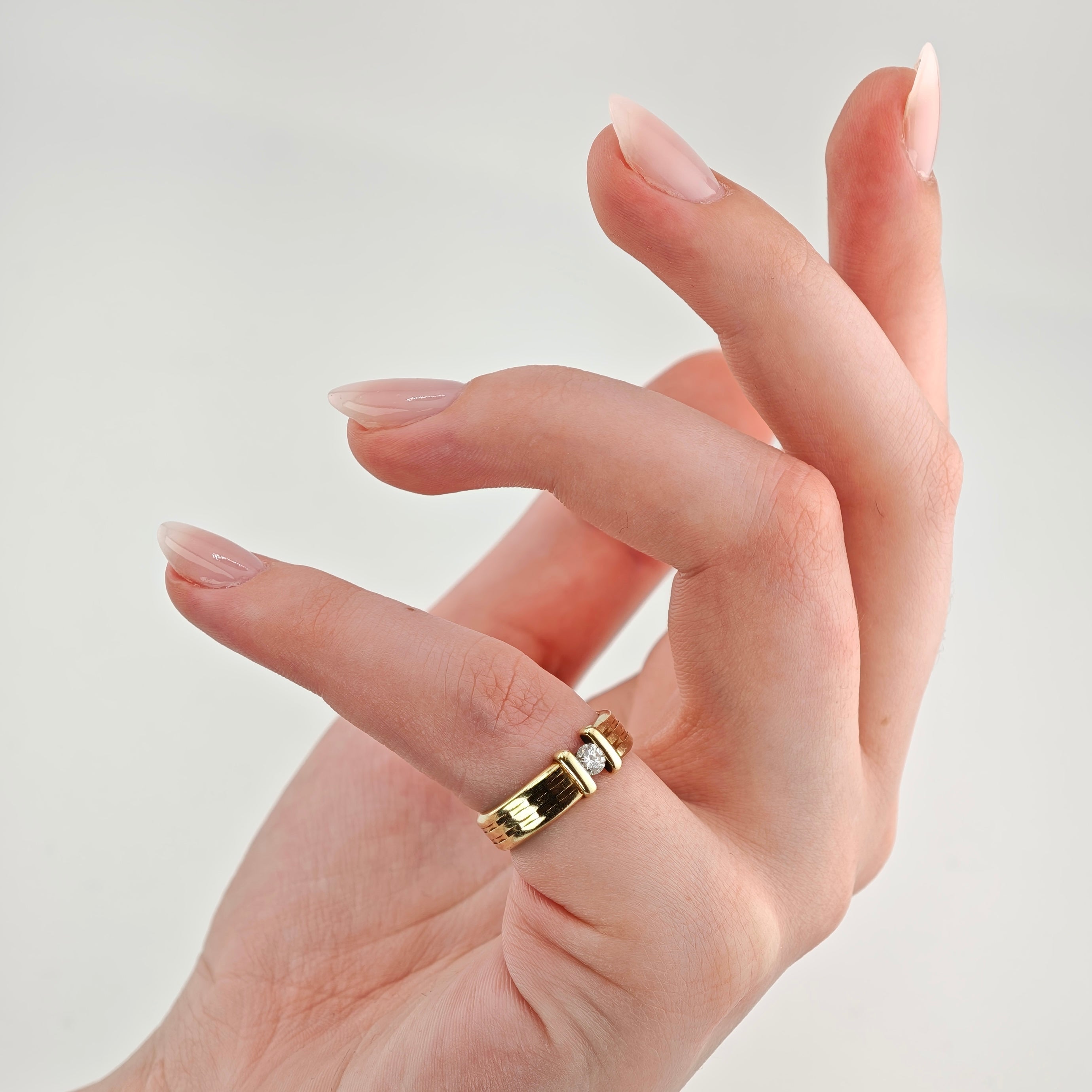 Hand mit elegantem Goldring am Zeigefinger, breiter Ring mit Diamant vor hellem Hintergrund.