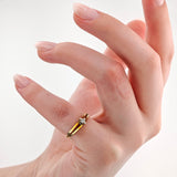 Hand mit hellrosa lackierten Nägeln und einem goldenen Ring mit kleinen funkelnden Steinen am Mittelfinger