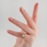 Hand mit gepflegten Nägeln und silbernem Ring mit herzförmigem cremefarbenem Schmuckstück vor hellgrauem Hintergrund