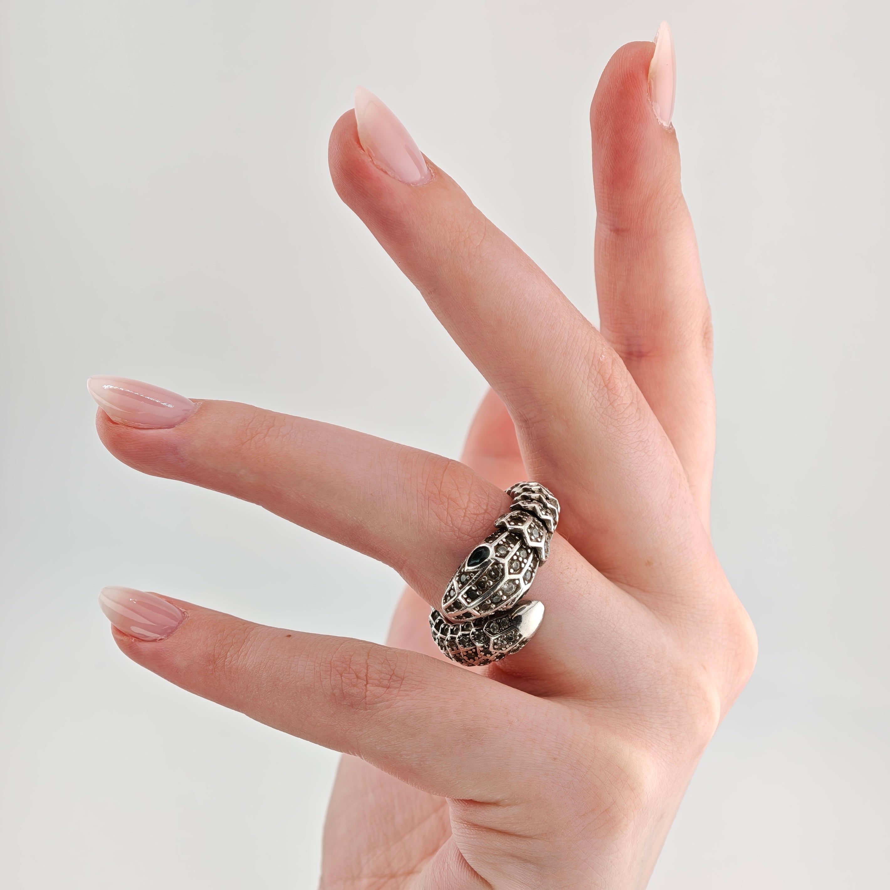 Hand mit hellrosa lackierten Nägeln und silbernem Schlangenring am Mittelfinger