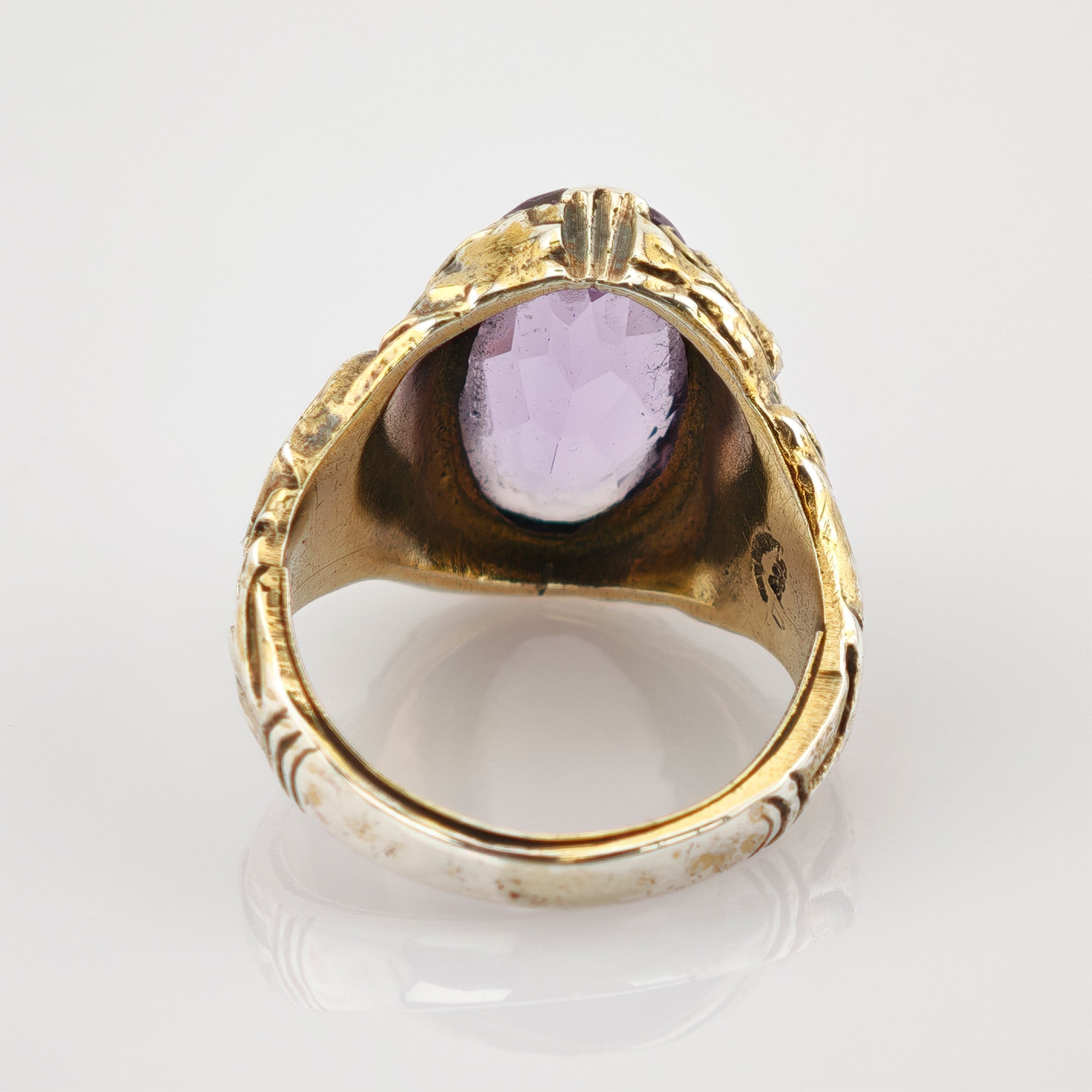 Innenansicht eines goldenen Rings mit facettiertem violettem Edelstein und eingraviertem Markenstempel