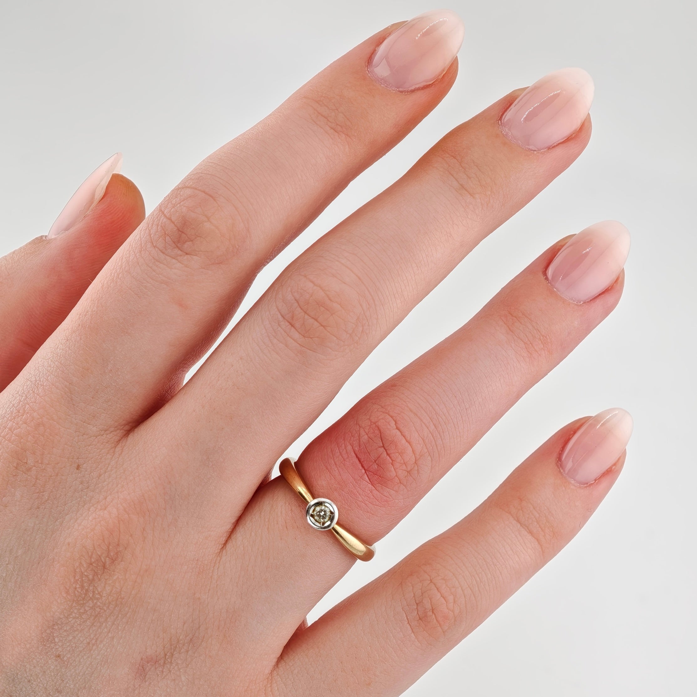 Linke Hand mit gepflegten, ovalen Nägeln in natürlichem Rosa und Goldring mit kleinem rundem Diamant am Ringfinger