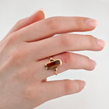 Linke Hand mit Goldring und rechteckigem Bernstein auf dem Ringfinger, hellrosa Maniküre, weißer Hintergrund.