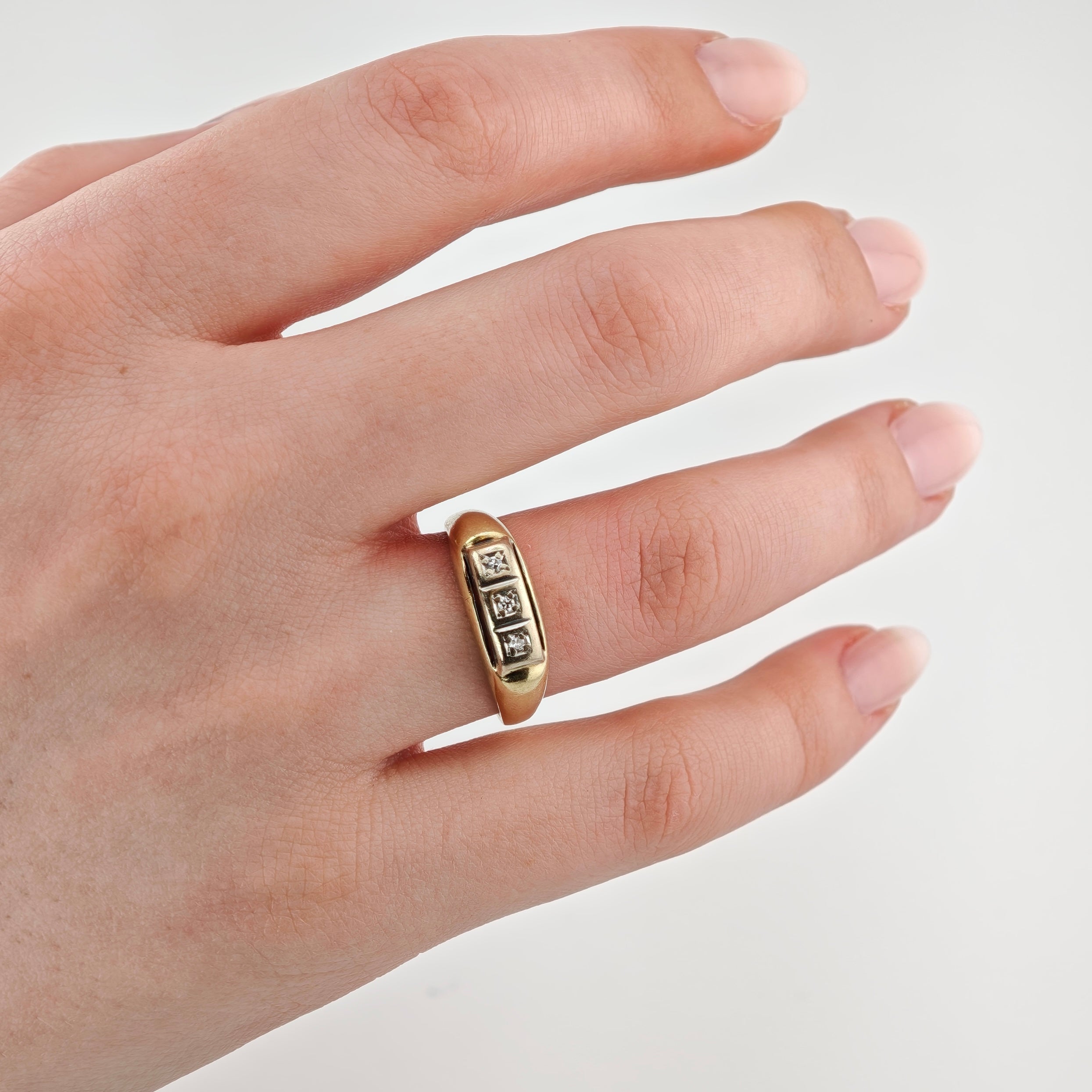 Linke Hand mit gepflegten Nägeln und Goldring mit drei Diamanten am Ringfinger auf weißem Hintergrund.
