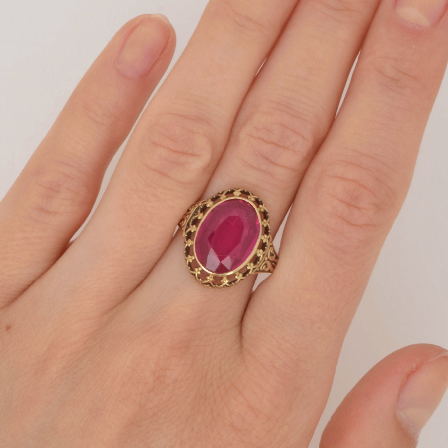 Linke Hand mit Goldring am Mittelfinger mit großem ovalem tiefrosa facettiertem Edelstein und verzierten Ringdetails.