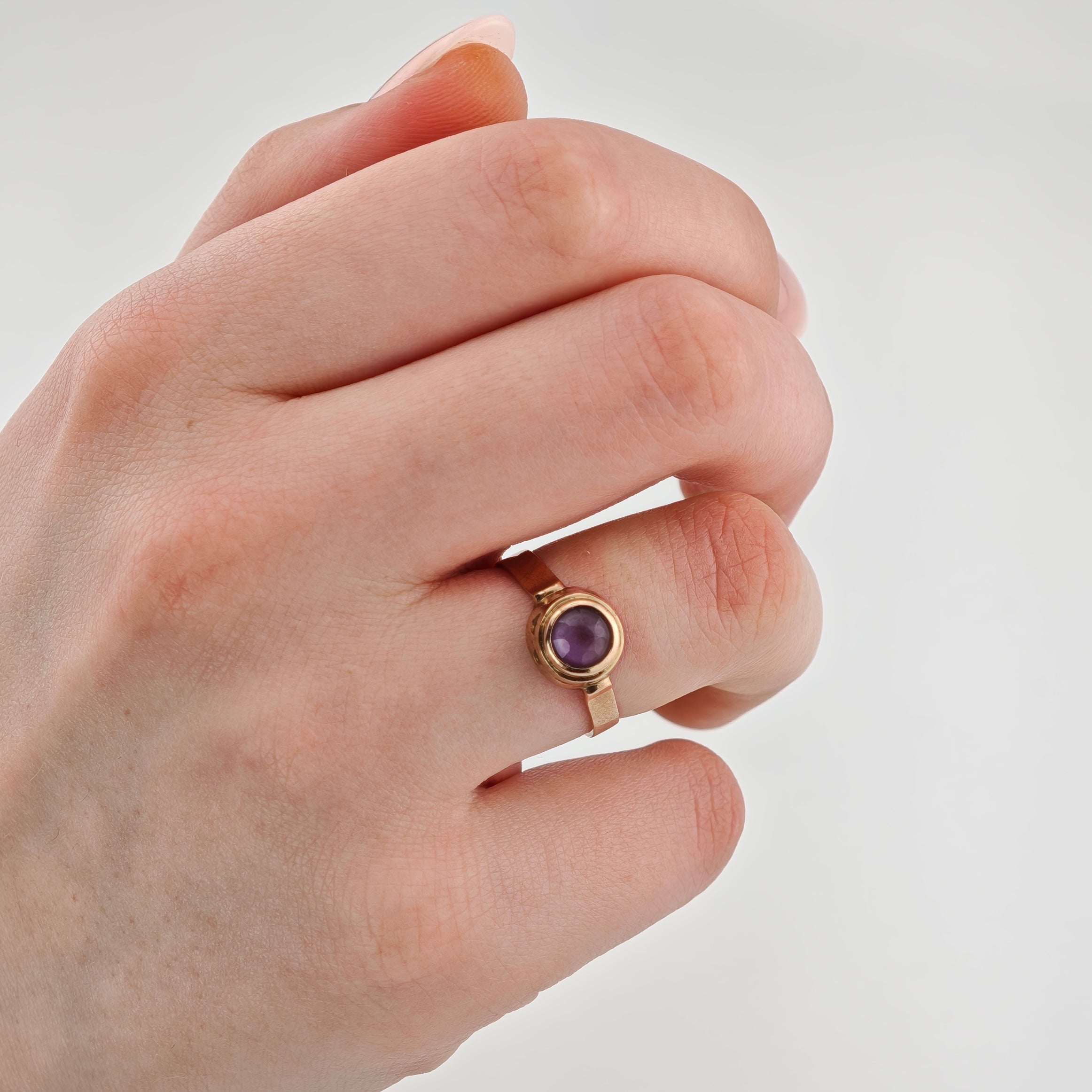 Linke Hand mit Goldring und rundem violettem Edelstein am Ringfinger.