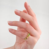 Linke Hand mit eleganten mandelförmigen rosa Nägeln und goldenem Ring mit grünem Marquise-Schliff Edelstein.