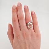 Linke Hand mit gepflegten, rosa lackierten Nägeln und modernem Silberring mit ovaler Verbindung am Ringfinger.