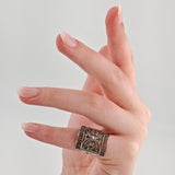 Linke Hand mit gepflegten Nägeln trägt breiten Silberring mit floralen und Spitzenmustern.