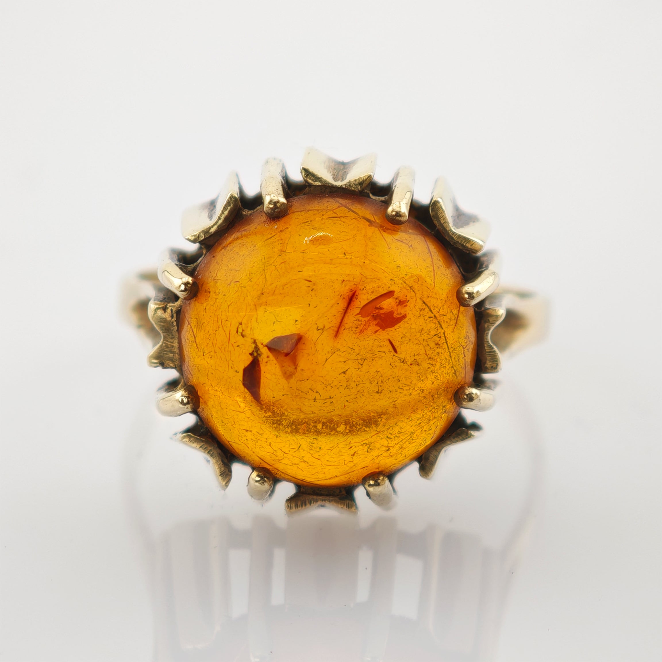 Makroaufnahme eines goldfarbenen Rings mit großem rundem Bernstein in kunstvoller Vintage-Fassung.