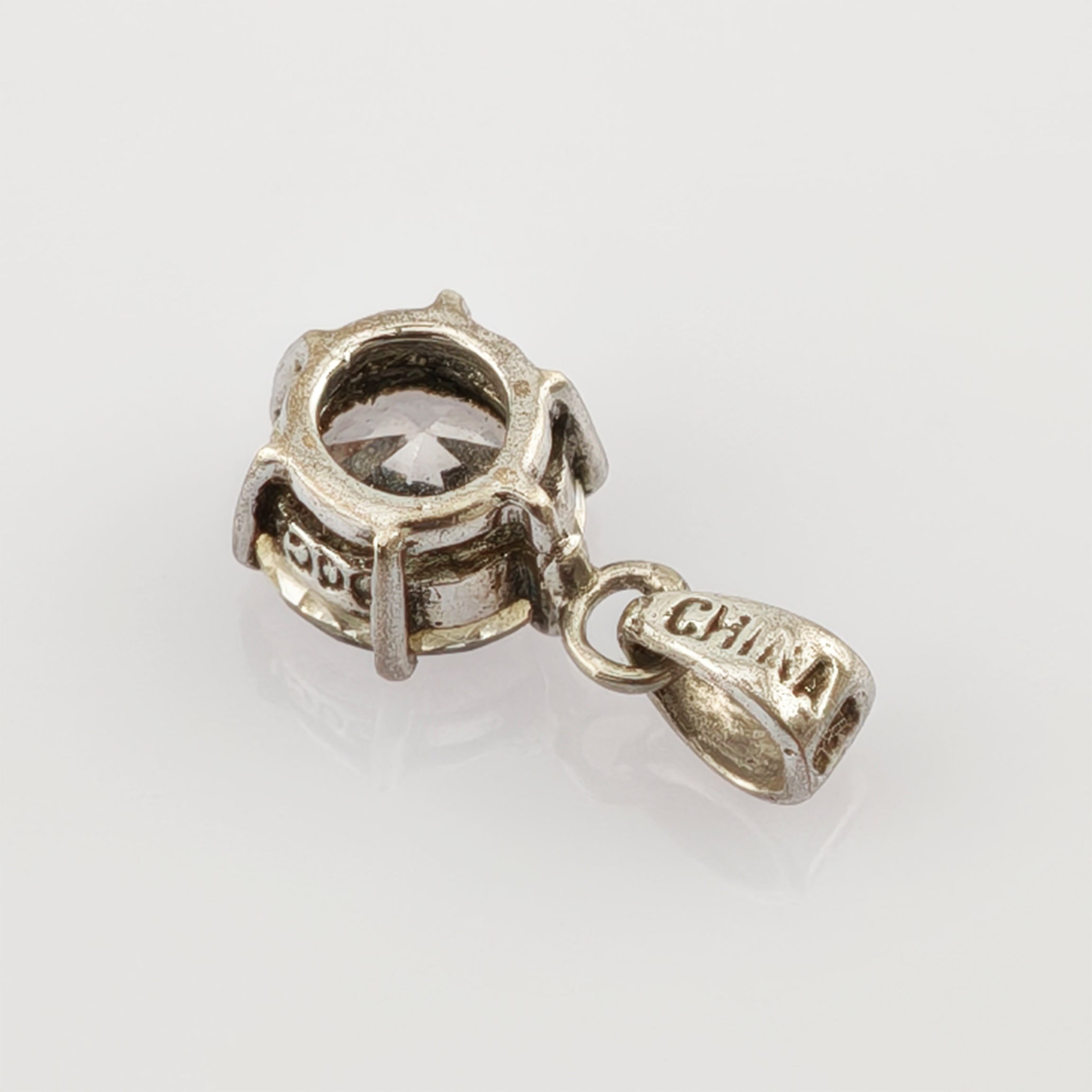 Metallanhänger mit klarem, rundem Edelstein und kleinem 'CHINA'-Anhänger auf weißem Hintergrund.