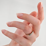 Nahaufnahme einer Hand mit gepflegten Nägeln und einem goldenen Ring mit klaren Edelsteinen am Mittelfinger