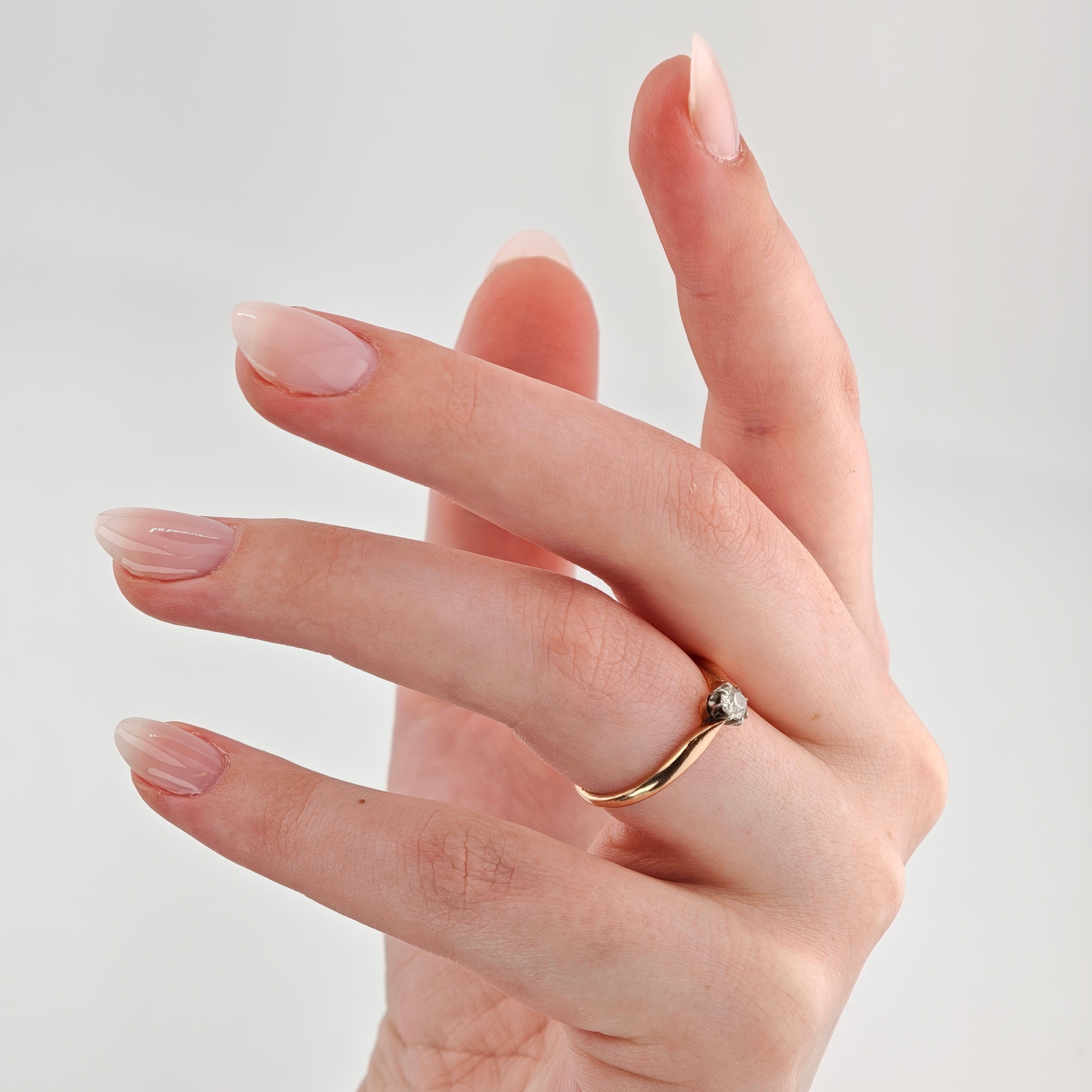 Nahaufnahme einer Hand mit goldenem Ring und kleinem Diamanten am Ringfinger, elegantes Vintage-Schmuckdetail.