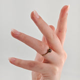 Nahaufnahme einer Hand mit pastellrosa Nägeln und Goldring mit violettem Edelstein am Mittelfinger