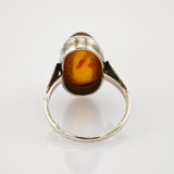 Nahaufnahme eines Silberrings mit ovalem Bernstein und rötlichen Einschlüssen, schlichtes Band mit leichter Abnutzung.