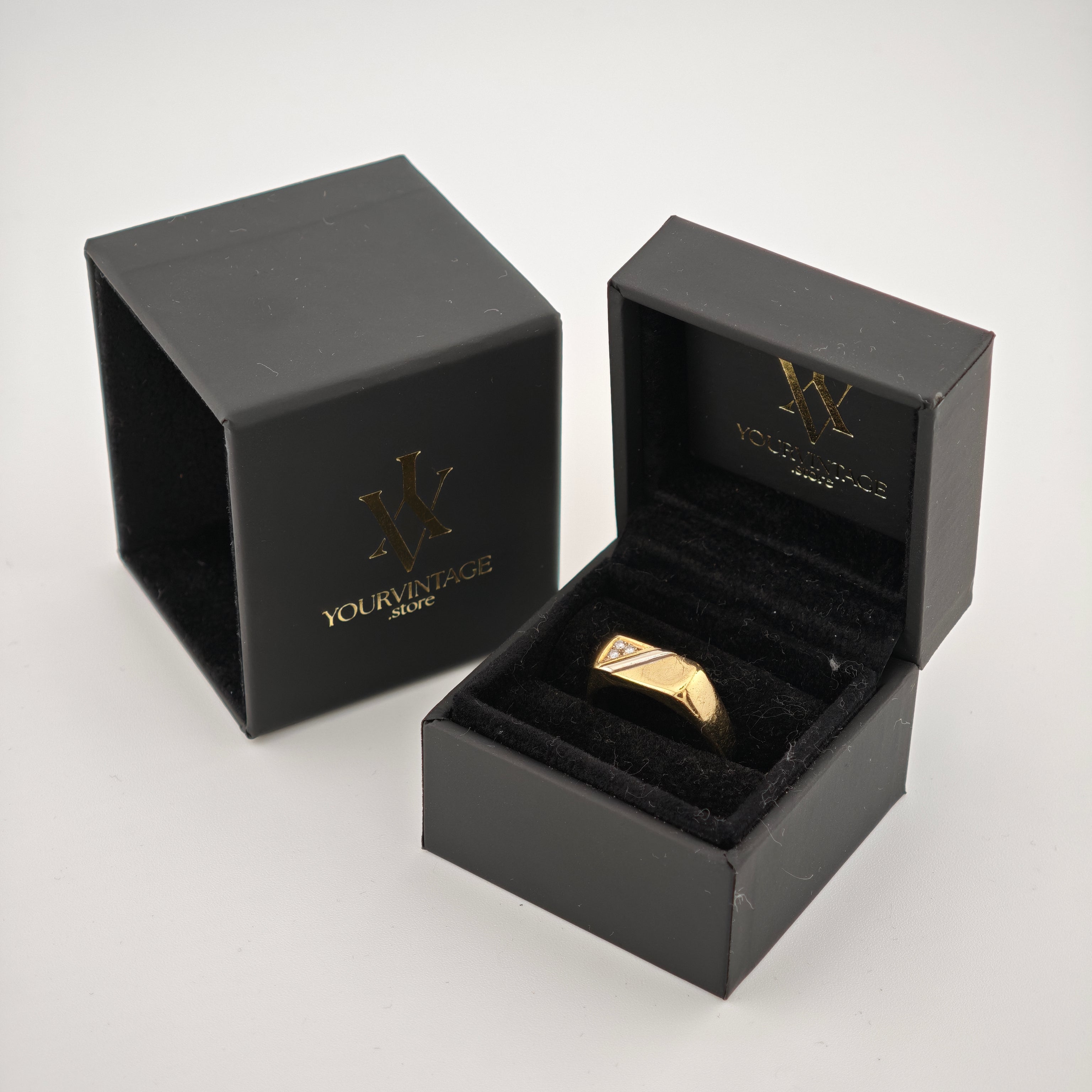 Offene schwarze Schmuckbox mit goldenem Ring auf schwarzem Samtkissen neben geschlossener Box mit Ihrem Vintage-Logo