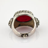 Ornamentaler Silberring mit eingravierten Mustern und großem roten Stein, floral verzierte Seiten.