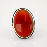 Ovalring mit poliertem rubinrotem Edelstein in Silberfassung auf weißem reflektierendem Untergrund.