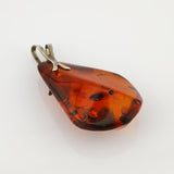 Polierter Bernsteinanhänger mit unregelmäßiger Tropfenform und natürlichen Einschlüssen in warmem Orangebraun.