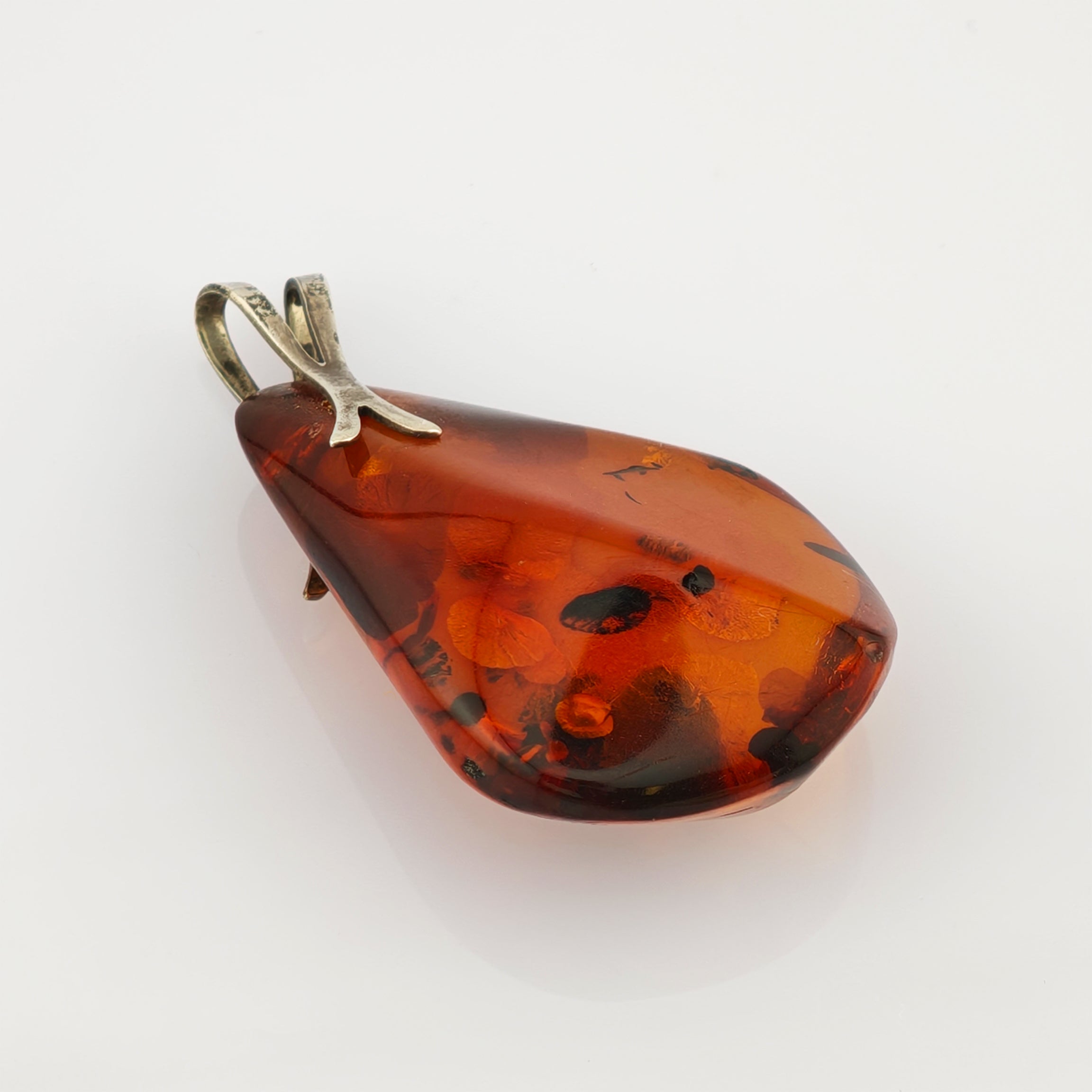 Polierter Bernsteinanhänger mit unregelmäßiger Tropfenform und natürlichen Einschlüssen in warmem Orangebraun.