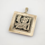 Quadratischer Metallanhänger mit leicht angelaufener Oberfläche und stilisierter Figur im Rahmen