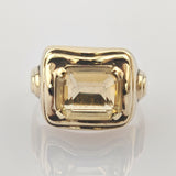 Goldener Ring mit großem rechteckigem gelbem facettiertem Stein in quadratischer Rechteckiger Goldring mit großem, facettiertem hellgelbem Edelstein, gehalten von vier Krappen, auf weißem Hintergrund.