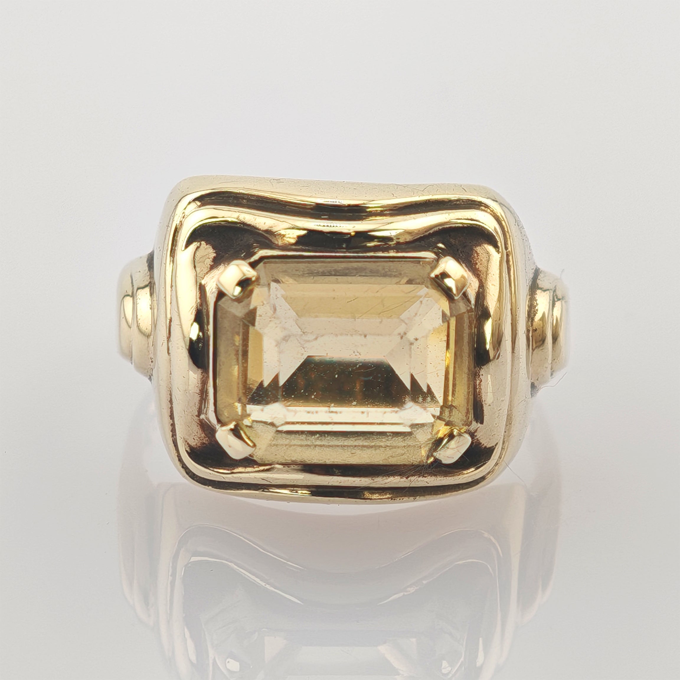 Goldener Ring mit großem rechteckigem gelbem facettiertem Stein in quadratischer Rechteckiger Goldring mit großem, facettiertem hellgelbem Edelstein, gehalten von vier Krappen, auf weißem Hintergrund.