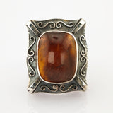 Rechteckiger Vintage-Ring mit poliertem braunem Bernstein und silbernem Rahmen mit Wirbelmustern.