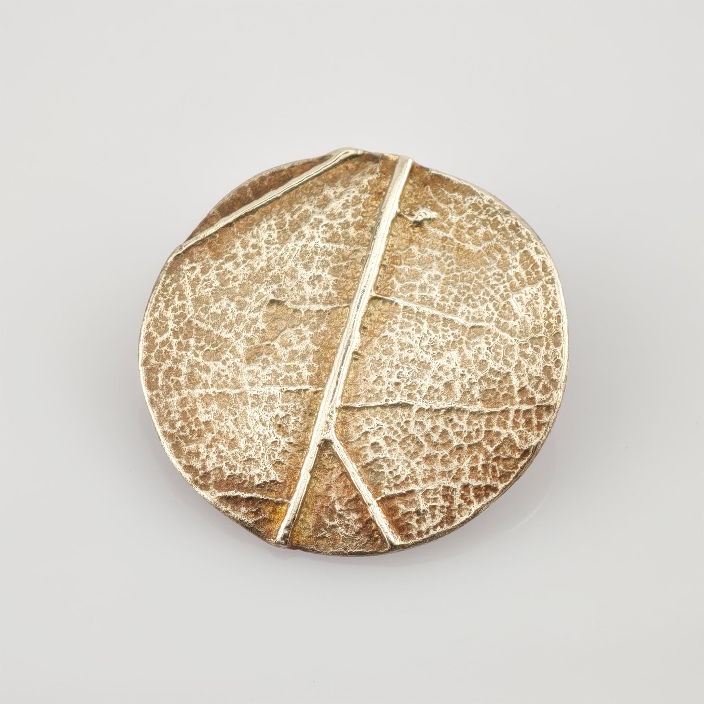 Rundes metallisches Objekt mit Blattaderstruktur in Gold und Bronze mit gealterter Patina.