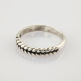 Ein schlichter silberner Ring mit geflochtenem Seilmuster auf weiß reflektierender Fläche.