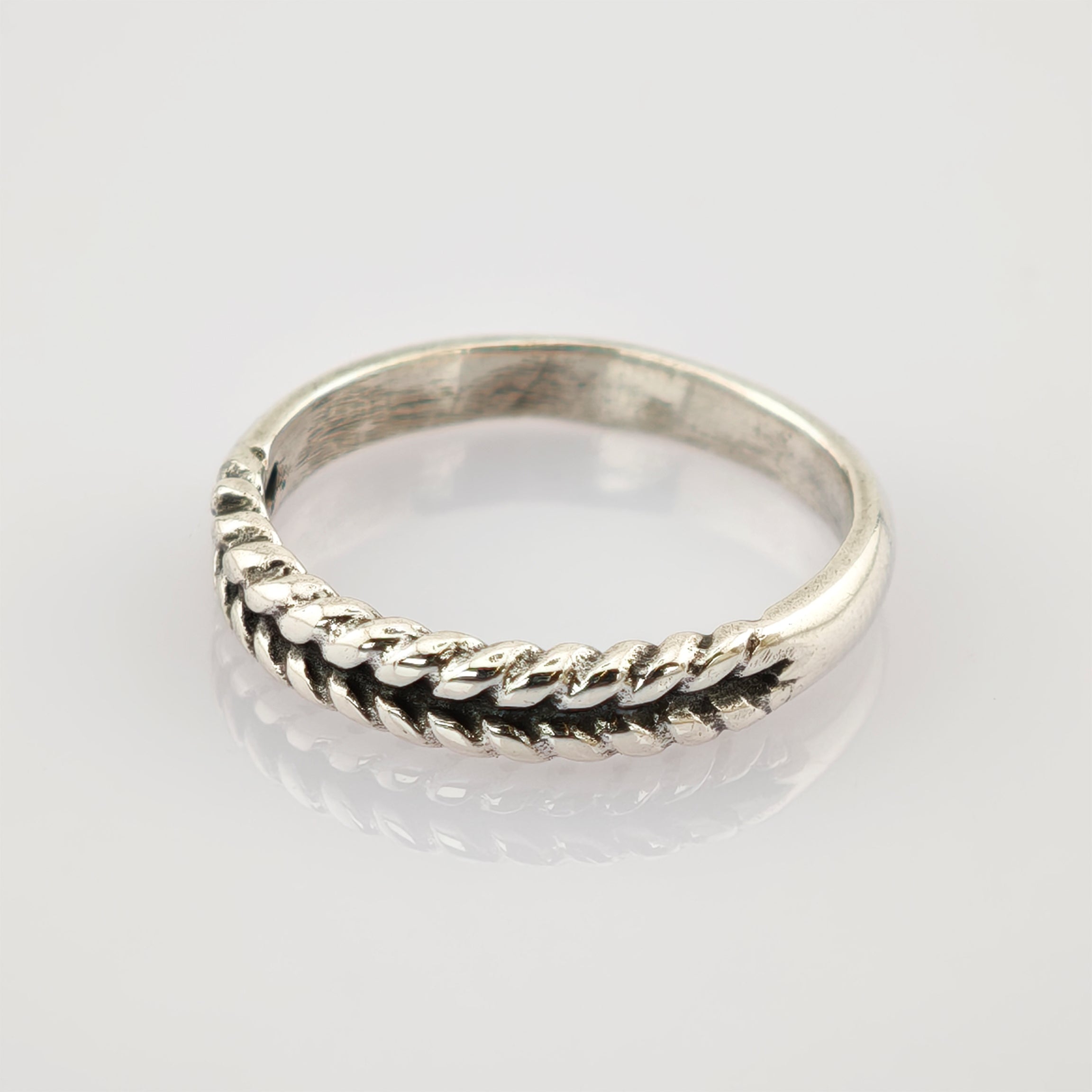Ein schlichter silberner Ring mit geflochtenem Seilmuster auf weiß reflektierender Fläche.