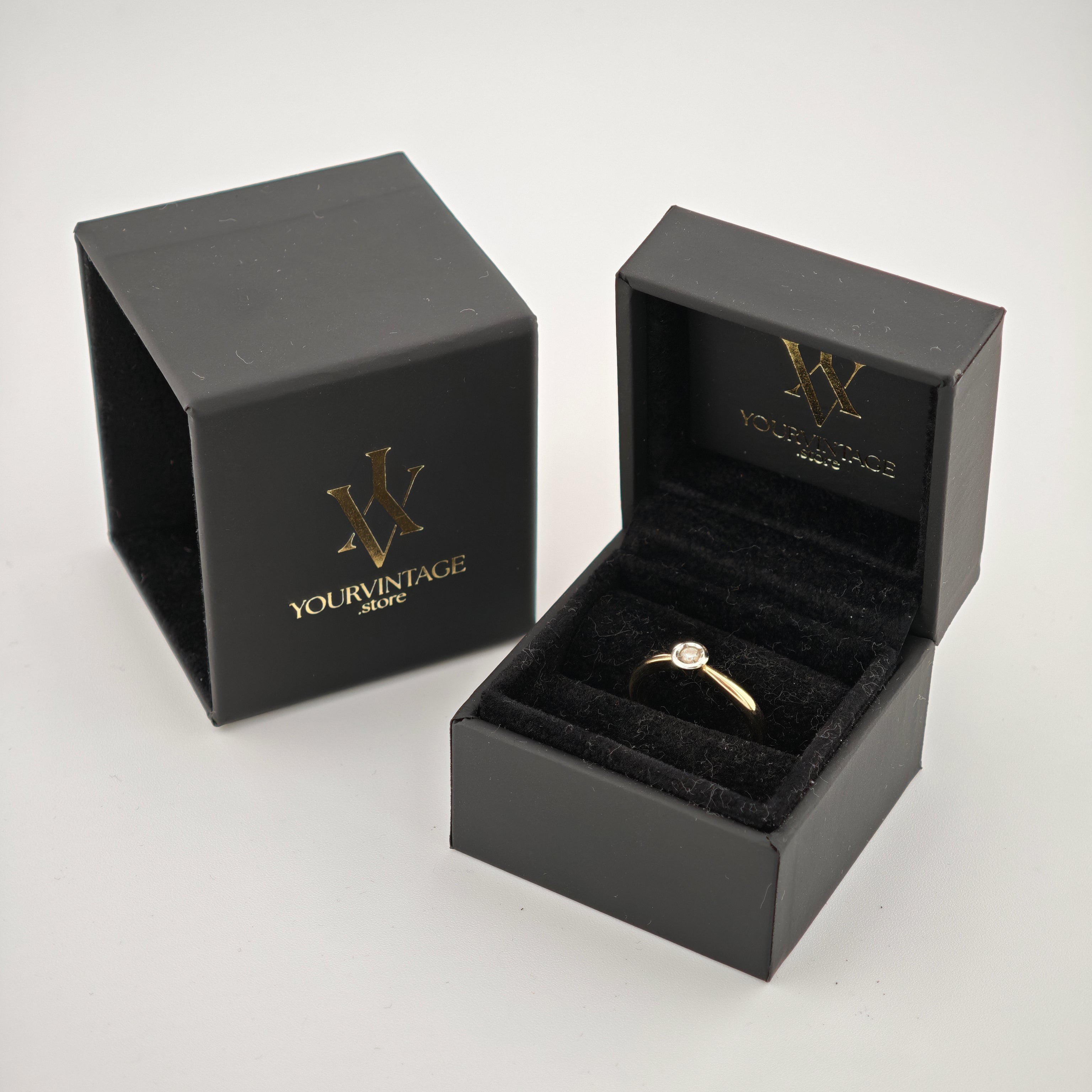 Schwarze Schmuckringbox mit goldfarbenem Ring und klarem Edelstein, daneben Box mit YOURVINTAGE-Logo.