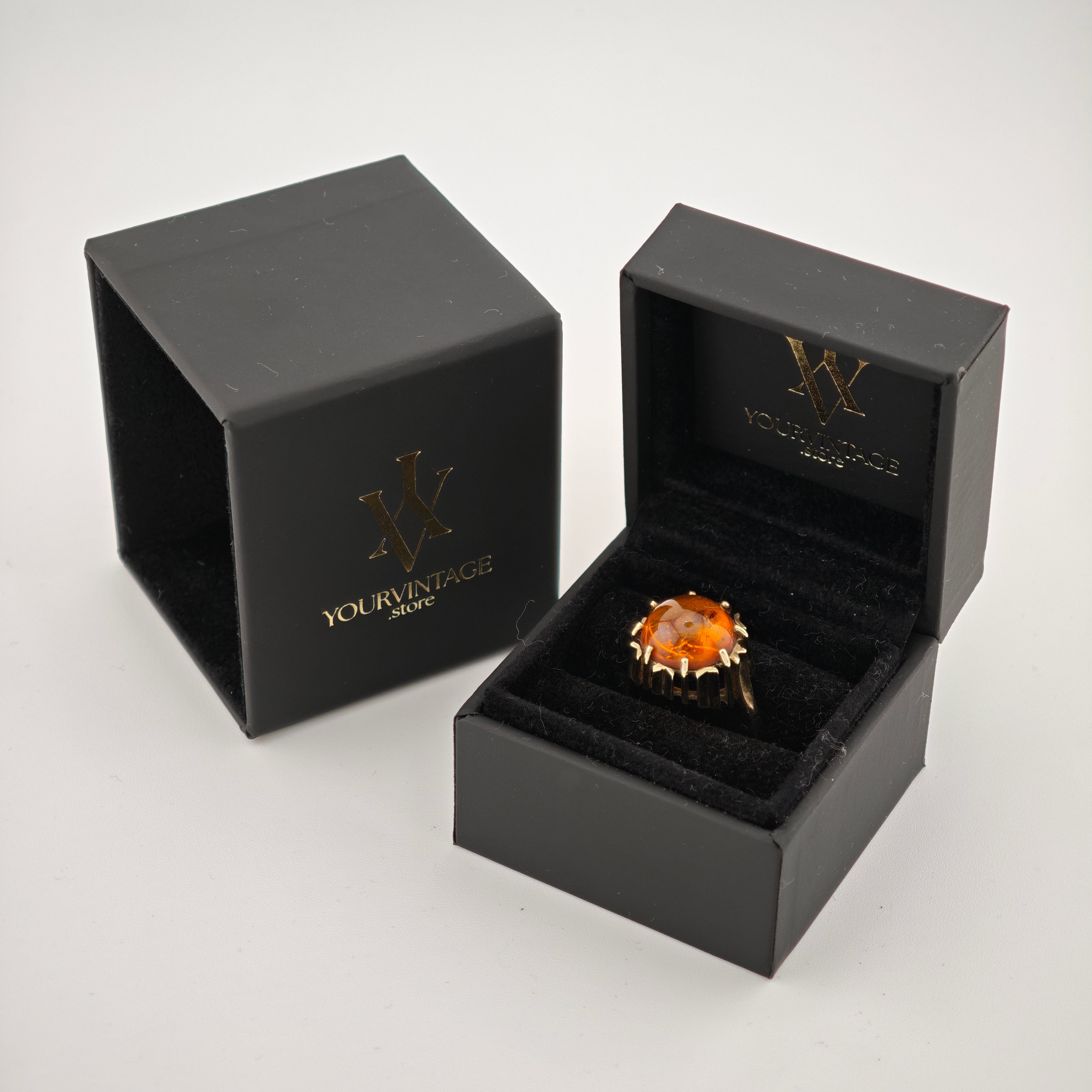 Schwarze Schmuckbox mit goldenem Ring und orangem Edelstein, Deckel mit YourVintage-Logo.