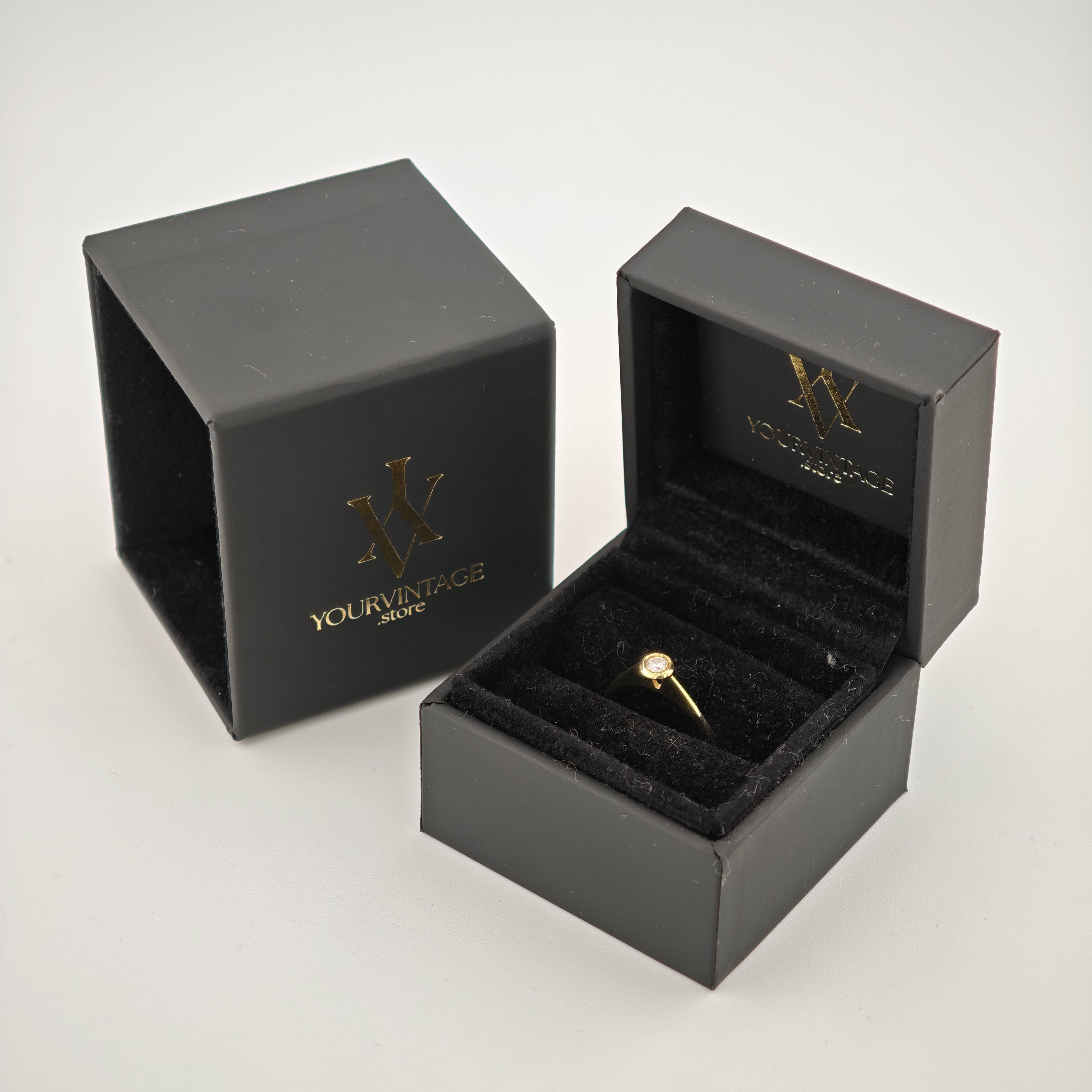 Schwarze Schmucketuis mit goldenem YOURVINTAGE Logo. Ein Etui offen mit Goldring und Diamant auf schwarzem Samtkissen.